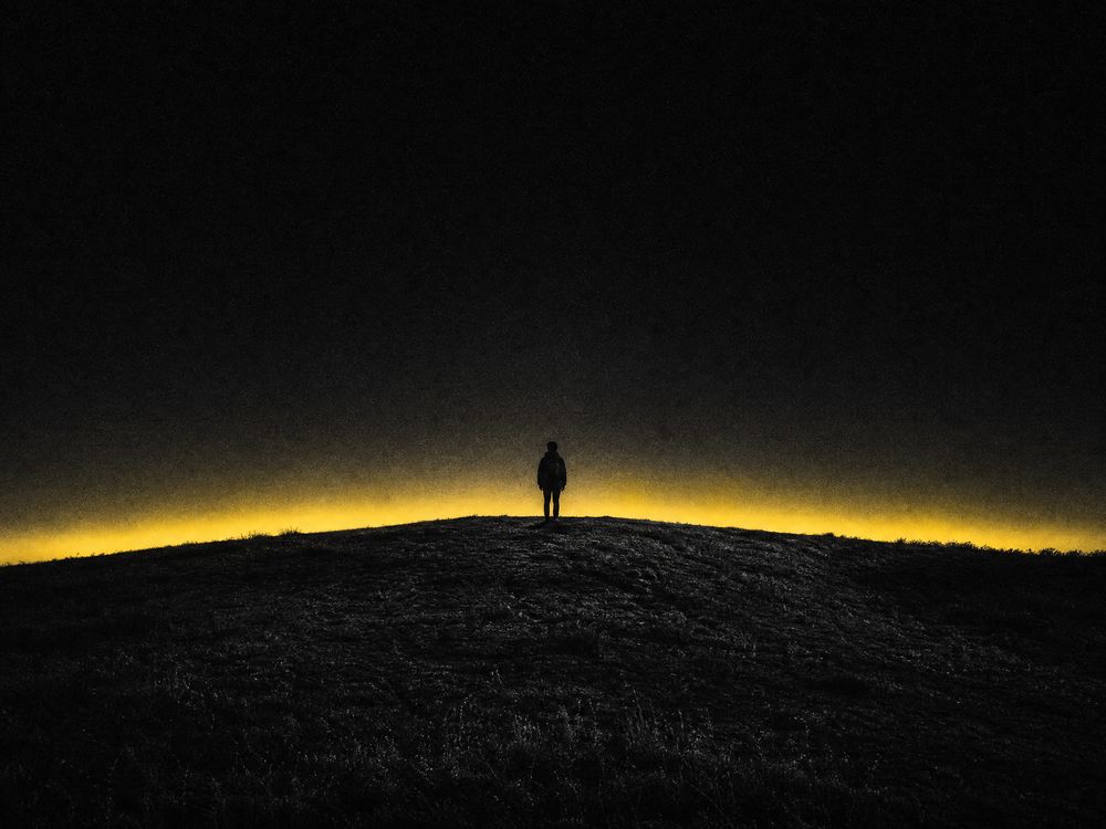 A monochrome landscape with a distant yellow horizon glow