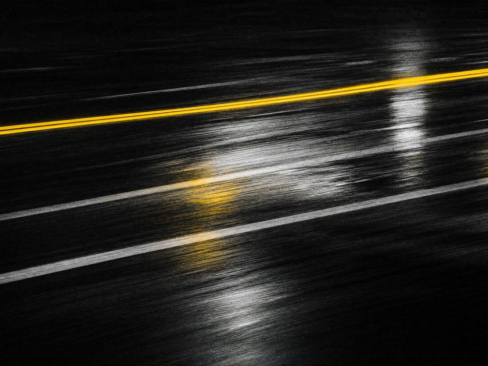 A wet monochrome road surface streaked with yellow reflected light