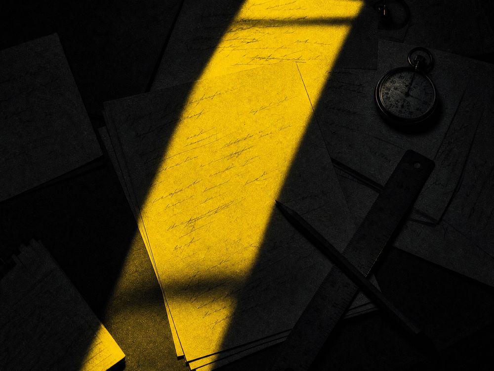 An overhead monochrome view of a table strewn with paper and one yellow-lit region